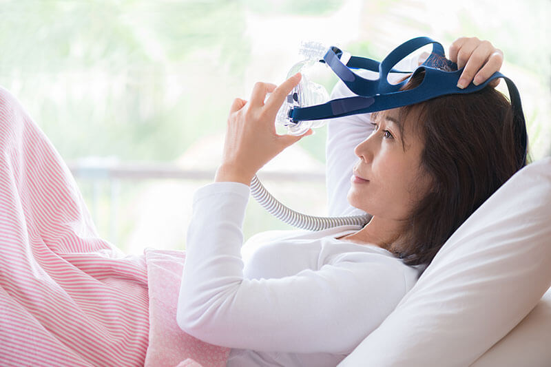a woman puts on her sleep apnea mask in bed