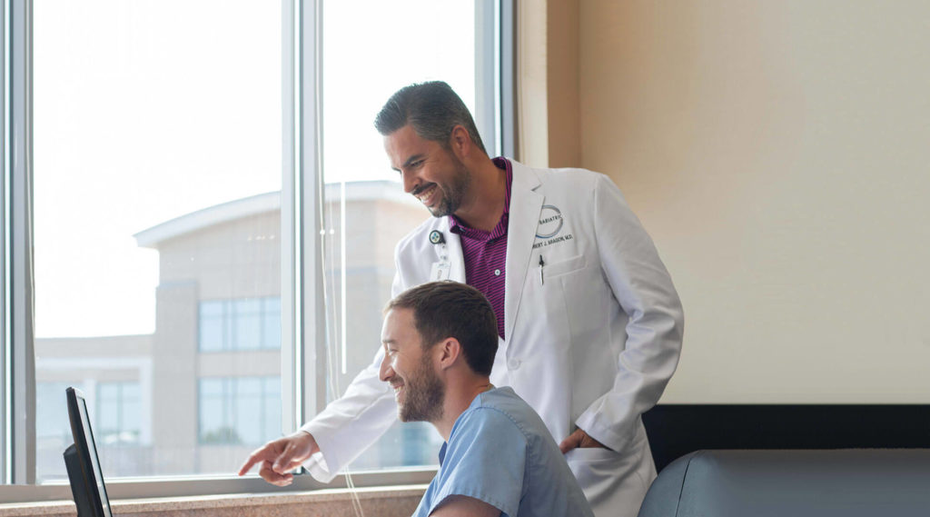 weight loss surgeon robert aragon smiles while pointing out computer screen to physician assistant jeff