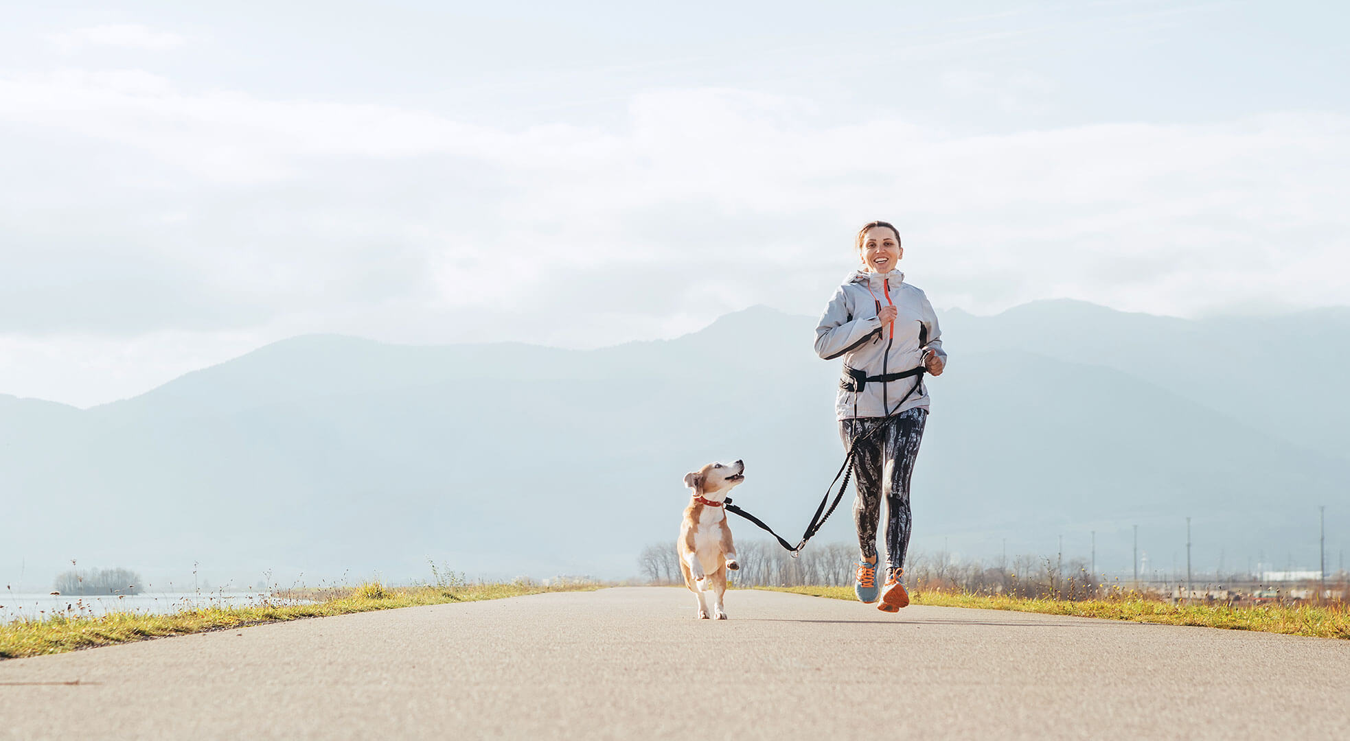 bariatric female patient runs with dog in front of mountains after successful weight loss surgery
