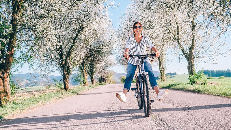 kc bariatric patient happily rides her bike on path with flowering trees