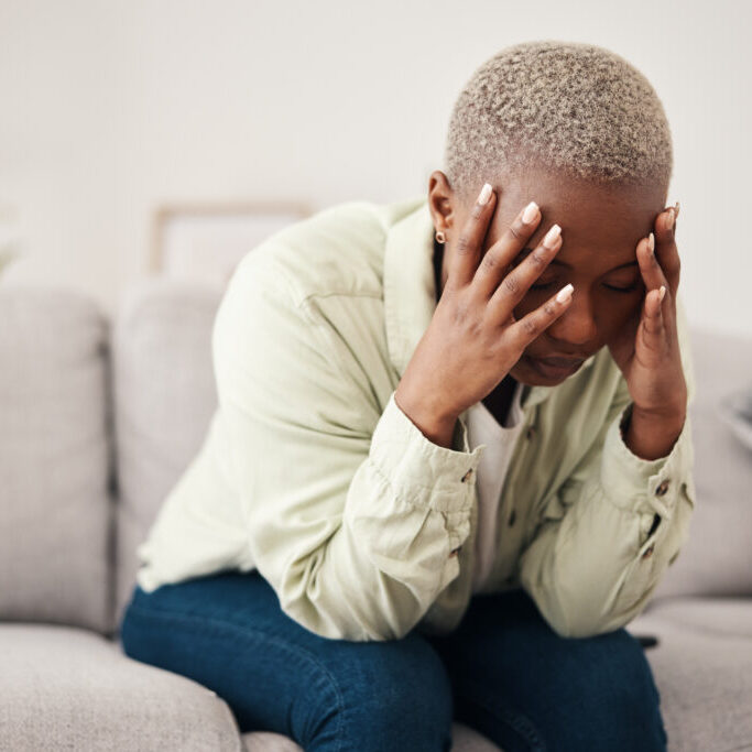 Stress, headache and vertigo with a black woman on a sofa in the living room of her home for mental.